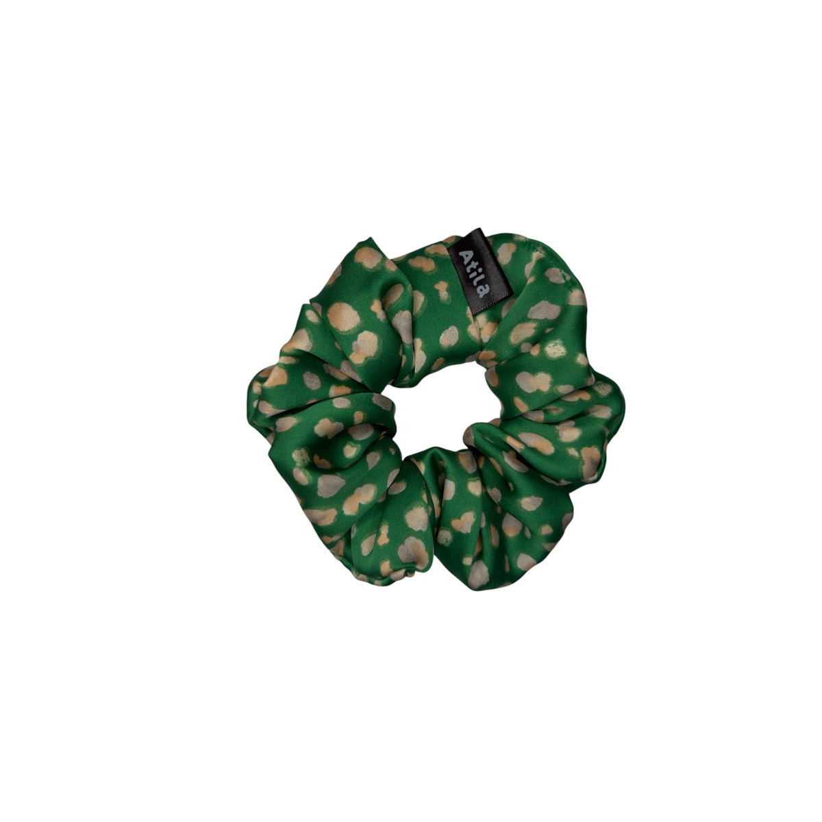 A green fabric scrunchie with a beige abstract dots print pattern and a black brand tag reading 'Atila' on a plain white background.